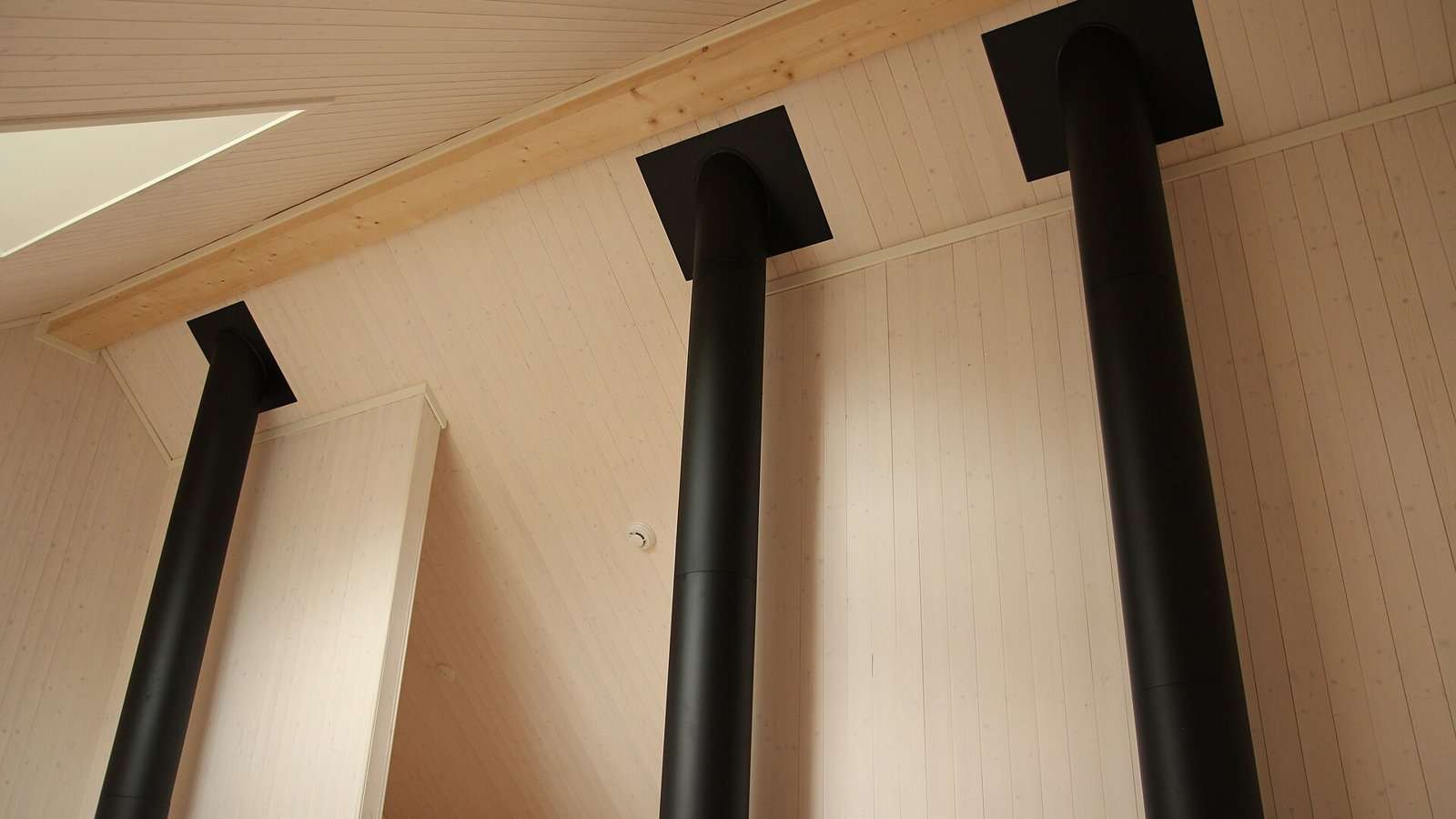 Sorte stålpiper ført opp gjennom et skrått tak i et nytt hus